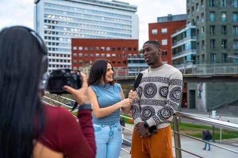 Reporter holding microphone and interviewing a young diverse man on a modern city street, while a