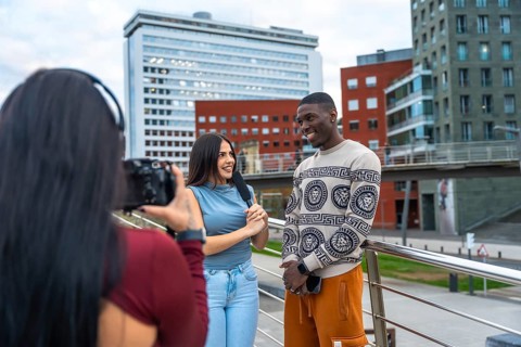 Journalist holding a microphone and talking with a smiling young man while a videographer is