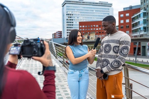 Journalist holding a microphone and interviewing a smiling young man on a modern urban bridge while