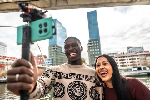 Diverse young couple vlogging together outdoors in a modern city, smiling and laughing as they live