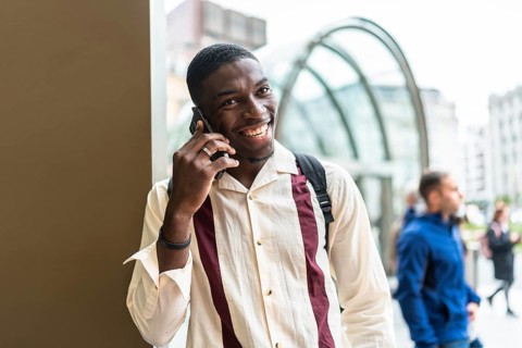 Smiling young black man talking on his mobile phone in an urban setting, enjoying a conversation