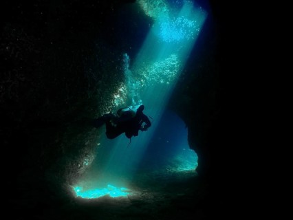 A diver floats through a mystical underwater cave, flooded with blue light. Fraskeric dive site,