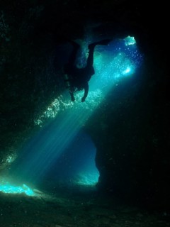 A dark cave is explored by a diver who is surrounded by dramatic rays of light. Fraskeric dive