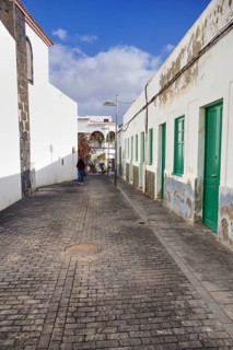 Narrow cobblestone street in Arrecife, Lanzarote, in portrait mode. On the left the back of the