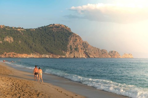 A couple walk along an empty Cleopatra Beach at sunset in the Turkish holiday resort town of Alanya