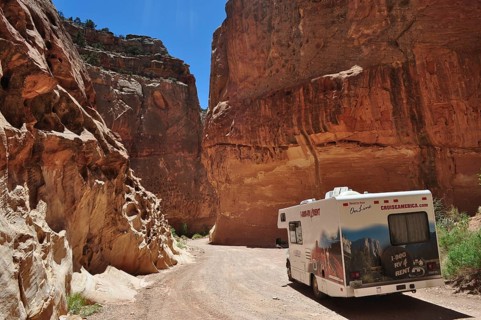 Motorhome traveling in a canyon with massive red rock structures under clear skies, Capitol Reef