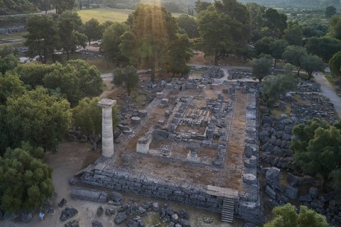 Temple of Zeus in backlight, aerial view of ruins under trees with a distinctive stone pillar in