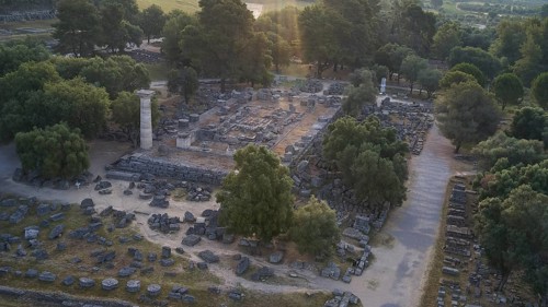 Temple of Zeus in backlight, ancient ruins surrounded by trees, with a single stone pillar amidst