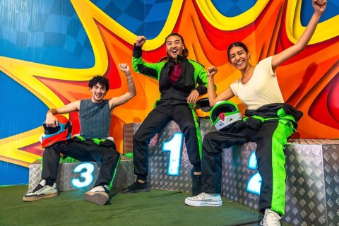 Three young multi ethnic friends on a karting podium, smiling and raising arms in victory while