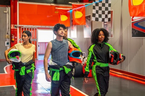 Diverse friends preparing for a go kart race, holding helmets and wearing race suits, walking