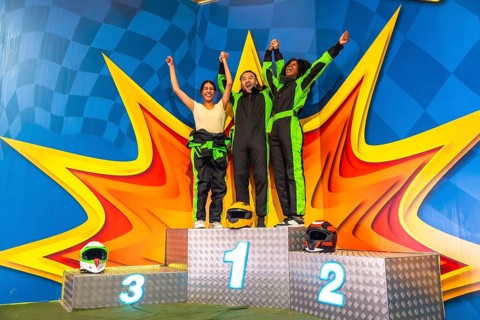 Three friends, dressed in race overalls, raising their arms and celebrating their achievement and