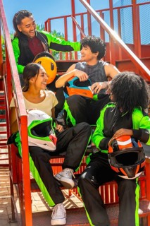 Happy diverse friends group wearing karting suits and helmets, sitting on metal stairs, laughing