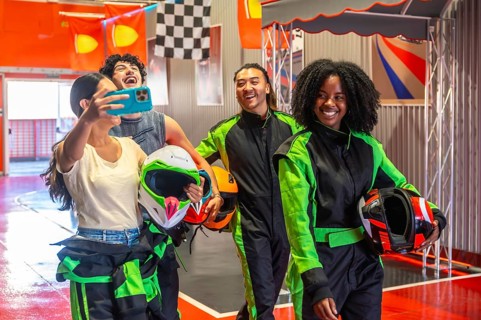 Diverse group of young adult friends wearing racing suits and holding helmets, posing for a