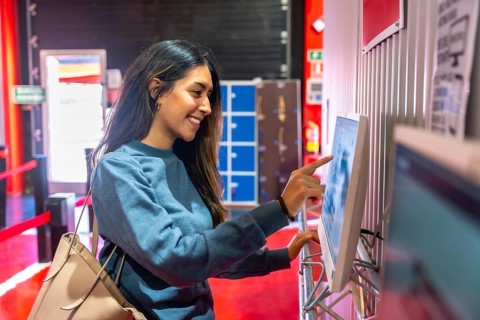Young woman smiling while interacting with a touchscreen display, checking in for a karting
