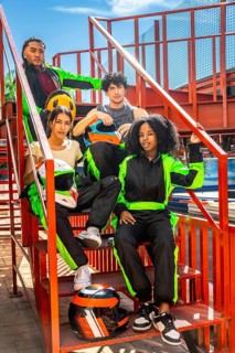 Group of diverse young people wearing racing suits and holding helmets, posing on metal stairs