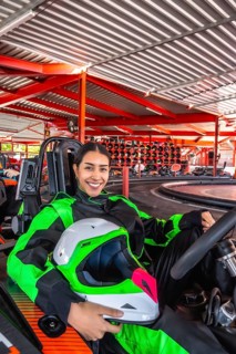 Young hispanic woman wearing a racing suit and holding a helmet, sitting in a go kart on the track,