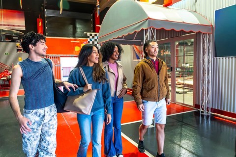Group of diverse young adult friends smiling, walking, and looking around at an indoor karting