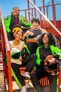 Diverse friends in racing suits holding helmets, smiling and sitting on red metallic stairs