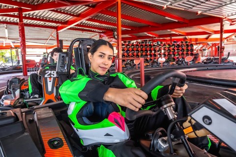 Woman in racing suit grips go kart steering wheel, seated on indoor track ready for competition,