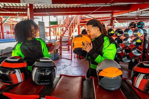 Diverse couple wearing racing suits, one partner kissing a helmet, getting ready for a go karting