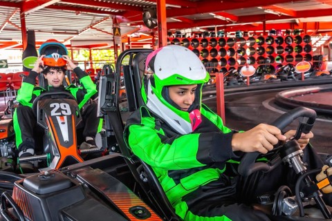Two young men, one putting on his helmet and another holding a steering wheel, are preparing for a