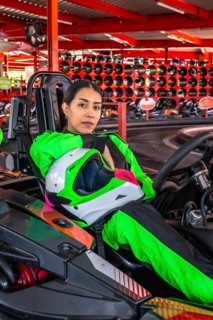 Young woman in a bright green racing suit holding a helmet and sitting in a go kart, ready for a