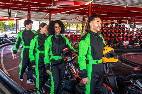 Group of diverse young adults wearing racing suits, carrying helmets, and smiling while walking