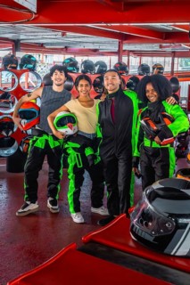 Group of diverse friends smiling and holding racing helmets, wearing go kart suits, and standing on
