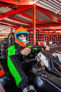 Young man wearing a racing suit and helmet, focusing on driving a go kart, preparing for a race at