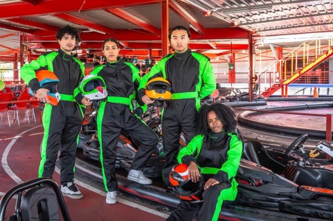 Diverse group of young adult friends standing in racing suits and holding helmets, preparing for a