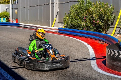 Person wearing a green racing suit and a yellow helmet is driving a go kart around a curve on an