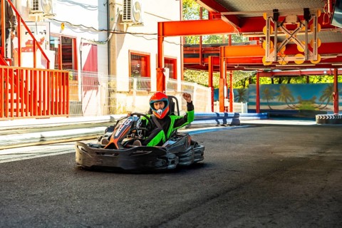 Go kart driver in helmet and racing suit crossing finish line on outdoor track, celebrating victory