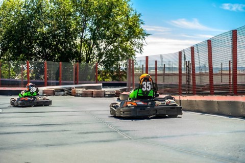 Two competitive go karts with drivers wearing helmets and number vests driving quickly on an