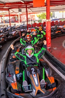 Group of excited people wearing helmets and racing suits, sitting in go karts and raising their