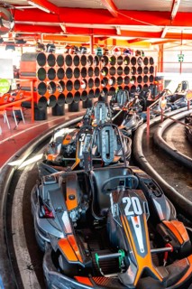 Go karts with orange and black details resting in a queue at the starting line of an indoor track,