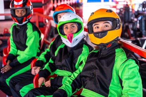 Young diverse friends in helmets and racing suits sit in go karts on an indoor track, ready and
