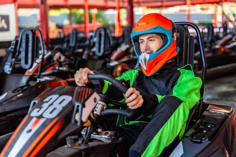 Man wearing an orange helmet and racing suit, sitting inside a go kart with the number 38, holding