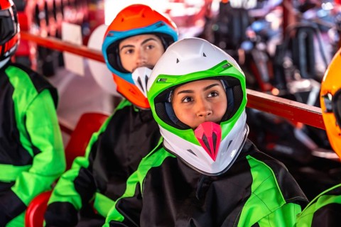 Young man and woman in racing suits and helmets sit in a go kart at the starting line, focused and