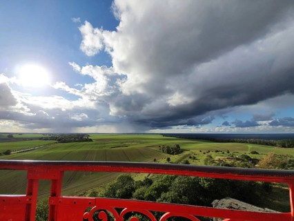 View of green fields under dramatic sky with dark clouds, red railings in the foreground and