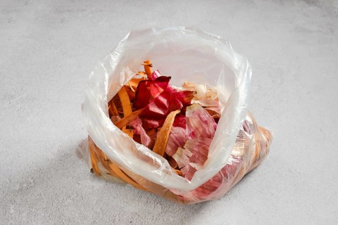A clear plastic bag on a kitchen counter, containing various vegetable scraps and peels. The bag