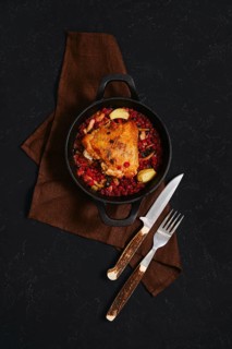 A chicken dish is served in a black cast iron pot. The pot contains spicy lingonberry sauce. Two