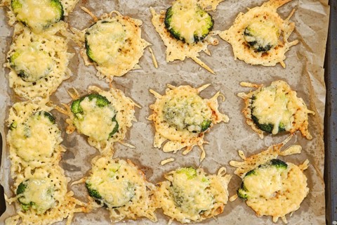 Broccoli pieces are smashed and spread on a baking sheet. They are topped with cheese and placed in