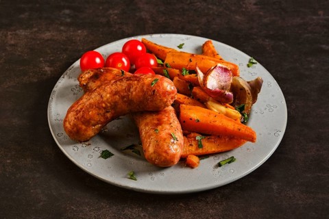A plate holds natural casing sausages alongside roasted sweet potatoes and cherry tomatoes. The