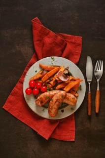 Natural casing sausages are placed on a green plate alongside roasted sweet potatoes and cherry