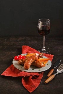 Natural casing sausages sit on a plate next to cherry tomatoes and roasted sweet potatoes. A glass