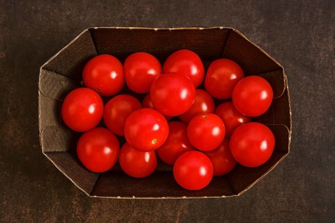 Cardboard box holds many red cherry tomatoes. The tomatoes are bright and round, placed together
