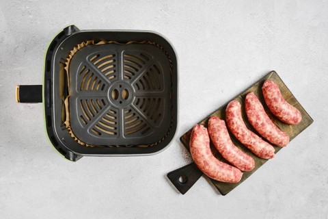 Fresh natural casing sausages on a cutting board beside an air fryer basket. The sausages are ready