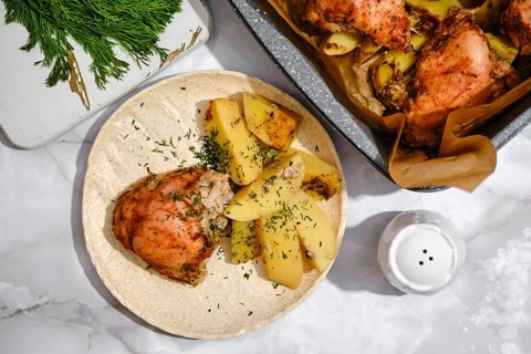 A plate holds pieces of chicken next to sliced and cooked potatoes. Fresh herbs are sprinkled on