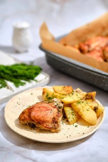 Roasted chicken and potato wedges. Baking tray is seen in the background with more chicken. The