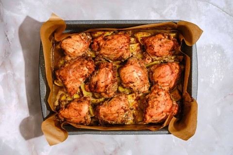 Baking tray with seasoned chicken thighs and sliced potatoes. The dish was roasted in an oven,